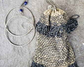May include: A vintage beaded bag with a silver chain and two blue glass beads. The bag is made of black and beige beads and has a fringe detail.