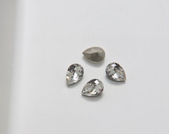 May include: Four clear teardrop-shaped crystal rhinestones and one gray teardrop-shaped rhinestone.