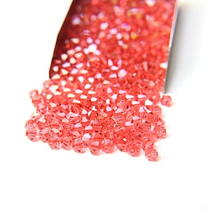 May include: A close-up of a pile of small, red, faceted glass beads. The beads are scattered on a white surface and appear to be spilling out of a container.