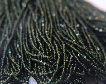May include: A close-up of a bundle of dark green seed beads with a slight shimmer. The beads are small and round, and they are arranged in a neat, organized pattern.