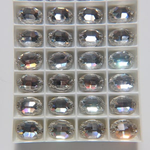 Puede incluir: Una bandeja de plástico transparente llena de piedras de cristal ovaladas transparentes. Las piedras tienen un acabado iridiscente arcoíris.