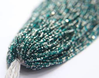 May include: A close-up of a strand of green and silver seed beads. The beads are small and round, and they are arranged in a tight, even pattern.