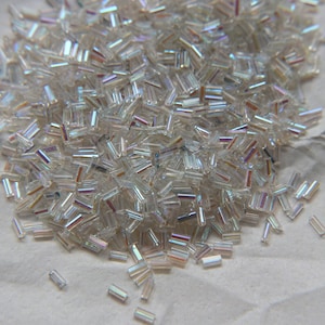 Op de afbeelding: Een stapel regenboogkleurige glazen kralen in een rechthoekige vorm. De kralen zijn helder met een regenboogkleurige glans.