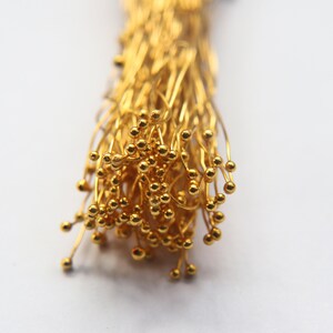 May include: A bunch of gold-colored wire with small round balls at the ends. The wire is twisted together to form a thick bundle.