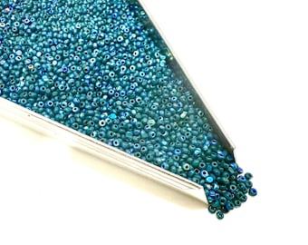 May include: A close-up shot of a silver tray filled with small, teal-colored beads. The beads are scattered, creating a textured surface. The beads are a mix of matte and iridescent finishes, reflecting light. Ideal for jewelry making and crafts.