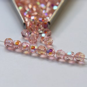 Puede incluir: Una hebra de cuentas de vidrio rosa iridiscente enhebradas en un alambre plateado. Las cuentas son facetadas y tienen un efecto brillante.