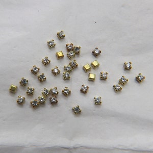 Peut inclure: Une collection de petits strass transparents et de d&eacute;corations en m&eacute;tal dor&eacute;. Les strass sont de forme carr&eacute;e et ont un design facett&eacute;. Les d&eacute;corations en m&eacute;tal sont &eacute;galement de forme carr&eacute;e et ont une finition lisse.