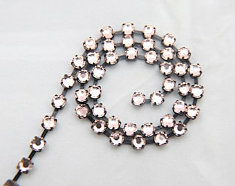 May include: A close-up of a black chain with small, clear rhinestones. The chain is coiled in a spiral shape.