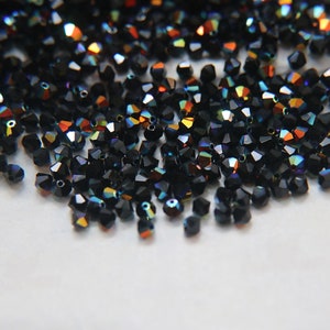 May include: A large quantity of black iridescent glass beads. The beads are faceted and have a rainbow sheen.