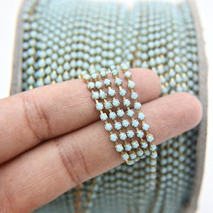 May include: A roll of light blue rhinestone chain trim. The chain is made of small, square rhinestones connected by gold metal links.
