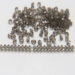 May include: A large quantity of small, dark grey glass beads, some of which are strung on a wire. The beads are faceted and have a shiny finish.