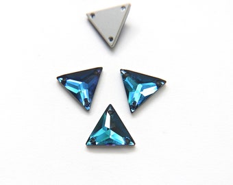 May include: Four triangular, faceted crystal rhinestones in shades of blue and teal. One rhinestone is a light gray color. Each has three small holes for attachment. The crystals are on a white background.