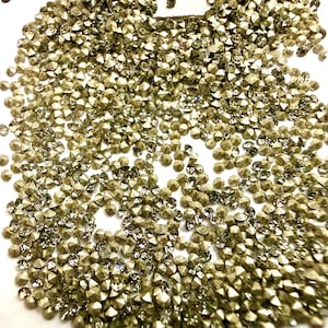 May include: A large collection of small, round, faceted rhinestones in a metallic gold hue. Each individual stone features a pointed top and a reflective surface, creating a dense, sparkling pile of loose embellishments for craft projects.