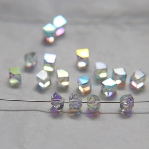 May include: A strand of iridescent glass beads strung on a silver wire. The beads are cube-shaped and have a rainbow-like sheen.