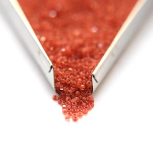 Puede incluir: Primer plano de una bandeja de metal llena de pequeñas cuentas redondas rojas. Las cuentas se derraman de la bandeja sobre una superficie blanca.