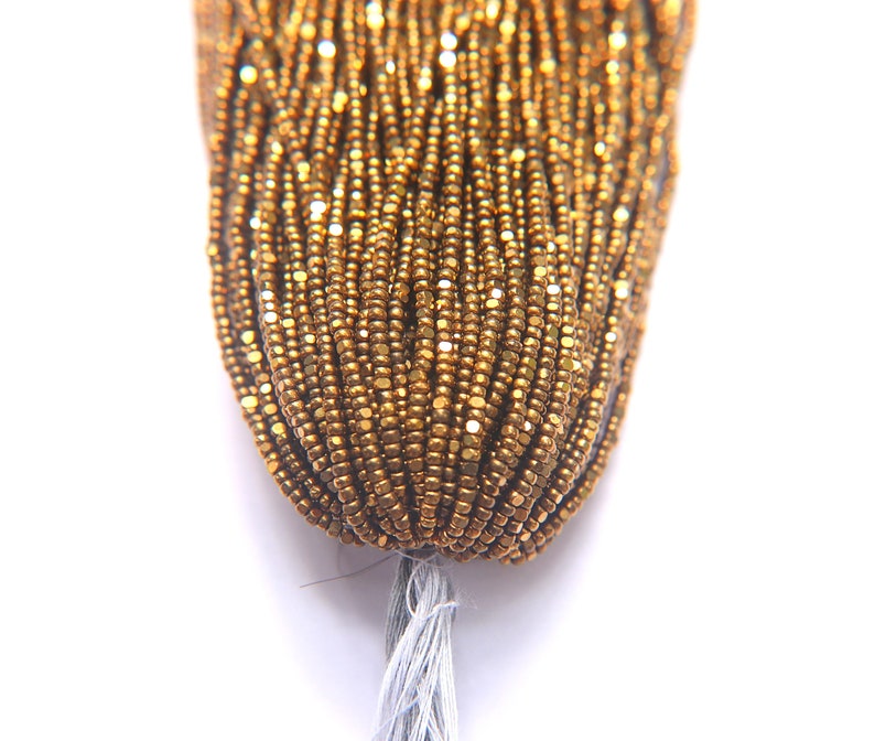 Puede incluir: Primer plano de un paquete de cuentas de semillas doradas. Las cuentas son peque&ntilde;as y tienen un ligero brillo met&aacute;lico.