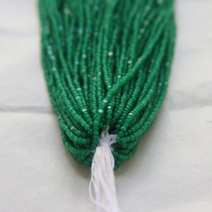 May include: A strand of green gemstone beads, likely jade, with a white string tied at the end. The beads are small and round, and they are arranged in a tight bundle.