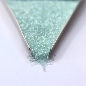 May include: A metal funnel filled with light blue glass beads, with some beads spilling out onto a white surface.