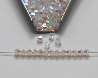May include: A strand of iridescent glass beads strung on a thin wire. The beads are small and have a faceted, diamond-like shape. A small metal container filled with loose beads is in the background.