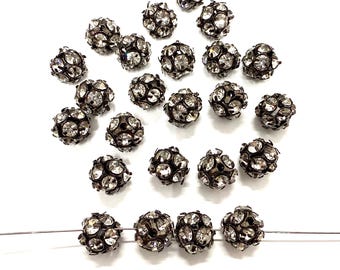 May include: A collection of silver-toned round beads with clear rhinestones. The beads are scattered on a white surface and some are strung on a wire.
