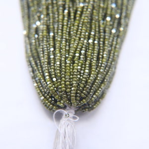 May include: A strand of green glass seed beads with a metallic sheen. The beads are small and uniform in size, and they are strung together on a thin thread.