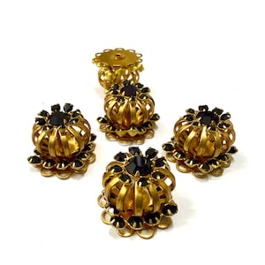 Può includere: Cinque orecchini a clip vintage in metallo dorato con un design floreale. Ogni orecchino presenta un gruppo centrale di pietre scure, possibilmente nere, circondate da una struttura a gabbia. Gli orecchini sono su sfondo bianco.