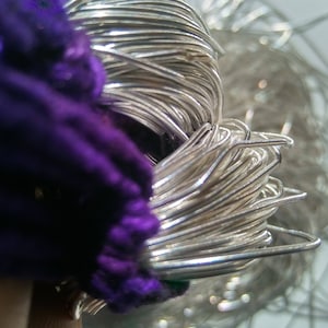 May include: A close-up of a bundle of silver wire, with a purple fabric in the background.