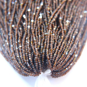 Peut inclure: Gros plan sur un paquet de perles de rocaille brunes avec un reflet argenté. Les perles sont petites et rondes, et elles sont disposées en un paquet serré.