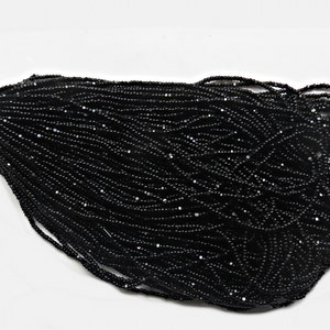 May include: A close-up of a pile of black seed beads. The beads are small and round, and they have a shiny finish.