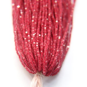 May include: A strand of red glass seed beads with a slight shimmer. The beads are small and uniform in size.