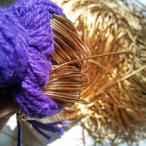 Könnte beinhalten: Nahaufnahme eines Bündels Kupferdraht neben einem Knäuel lila Garn. Der Kupferdraht ist aufgerollt und hat ein glänzendes, metallisches Aussehen. Das Garn ist tiefviolett und hat eine weiche Textur.