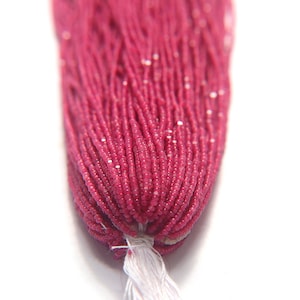 May include: A strand of pink gemstone beads, approximately 2mm in diameter, strung on a white thread.