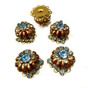 Può includere: Un assortimento di componenti di gioielli vintage. I pezzi includono cinque componenti in metallo color rame ornati con strass azzurri. Un pezzo è un attacco a vite. Gli altri quattro sono elementi decorativi.