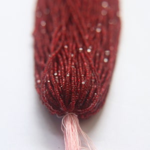 May include: A strand of red seed beads with a white iridescent finish. The beads are strung on a thread and tied together at the end.