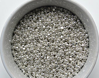 May include: A bowl filled with silver-colored round beads. The beads are small and uniform in size.