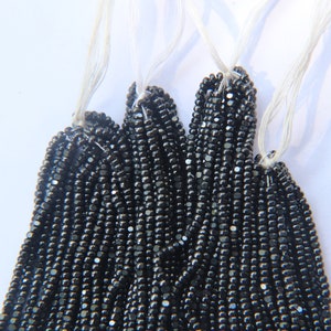 May include: A strand of black seed beads, strung on white thread. The beads are small and round, and they have a slightly iridescent finish.