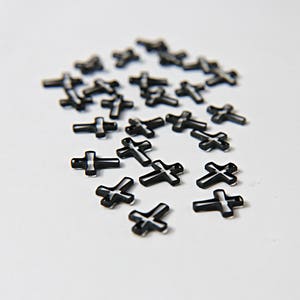 Peut inclure: Une dispersion de croix acryliques noires avec un contour blanc. Les croix sont petites et délicates, et elles sont disposées de manière aléatoire sur un fond blanc.