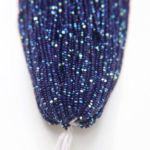 Può includere: Primo piano di una striscia di perline di semi iridescenti blu scuro. Le perline sono piccole e rotonde, e hanno un leggero luccichio.