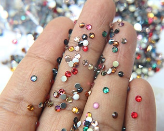May include: Assortment of colorful rhinestones in various sizes and shapes, displayed on a hand. The rhinestones are a mix of clear, red, green, black, and brown.