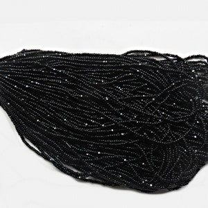 May include: A close-up of a pile of black seed beads. The beads are small and round, and they have a slightly iridescent finish.