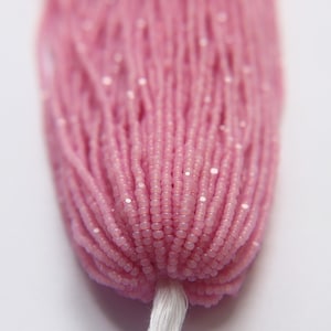 May include: Close-up of a bundle of pink seed beads. The beads are strung together, forming a dense, textured mass. The color is a soft, muted pink, with a slight sheen. The beads are held together by a white string.