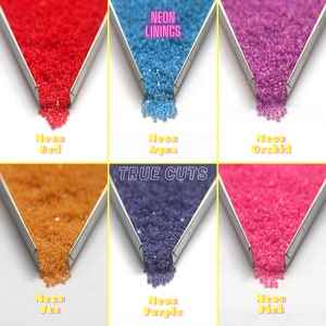 Op de afbeelding: Assortiment van neonkleurige zaadkraaltjes in verschillende kleuren, waaronder rood, aqua, orchidee, zon, paars en roze. De kralen worden gepresenteerd in kleine metalen bakjes met de woorden "Neon Linings" en "True Cuts" gedrukt boven de bakjes.
