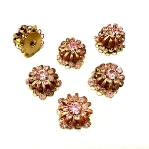 Può includere: Sei orecchini vintage a clip. Gli orecchini presentano un design floreale con strass rosa incastonati in metallo dorato. Gli orecchini sono disposti su sfondo bianco.