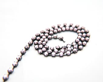May include: A strand of light pink rhinestones connected by black metal links. The rhinestones are round and have a faceted finish.