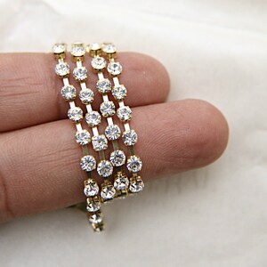 May include: Gold rhinestone chain trim with clear rhinestones. The chain is coiled and held in a hand.