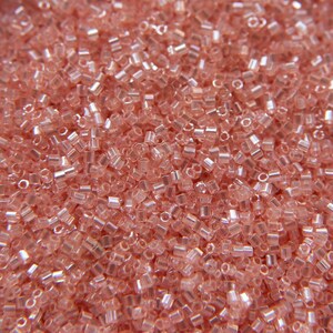 Può includere: Una vista ravvicinata di una grande quantità di piccole perline di seme rosa traslucide. Le perline hanno una finitura leggermente iridescente, che conferisce loro un bagliore sottile.