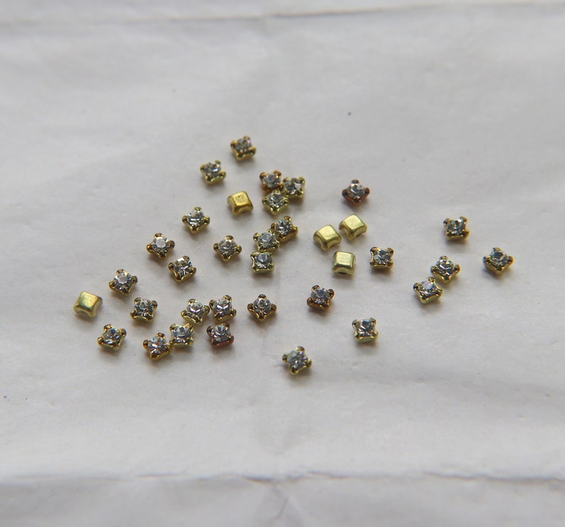 Peut inclure: Une collection de petits strass carr&eacute;s avec des montures dor&eacute;es. Les strass sont transparents et ont un l&eacute;ger &eacute;clat.
