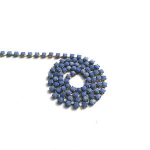 May include: A close-up of a blue rhinestone chain, coiled into a circle. The chain is made of small, square rhinestones that are connected by gold metal.