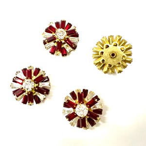 Può includere: Quattro orecchini vintage. Tre orecchini presentano un cristallo centrale trasparente circondato da strass rossi e trasparenti taglio baguette. Il quarto orecchino è dorato con un design a raggiera. Il tutto su sfondo bianco.