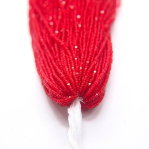 Puede incluir: Primer plano de un paquete de cuentas de semillas rojas con un hilo blanco atado al final.